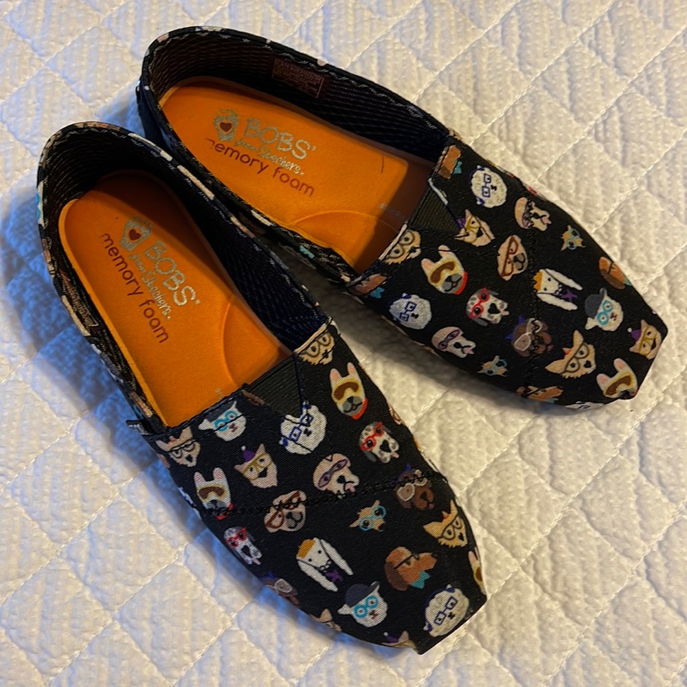 BOBS By Skechers slip on shoes in black with various dog designs on the shoes.